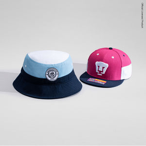 Manchester City Truitt Bucket hat on left and Pumas Truitt Snapback hat on right, in a tonal grey environment.