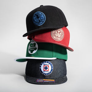Stack of Fan Ink Snapbacks featuring teams from Liga MX.